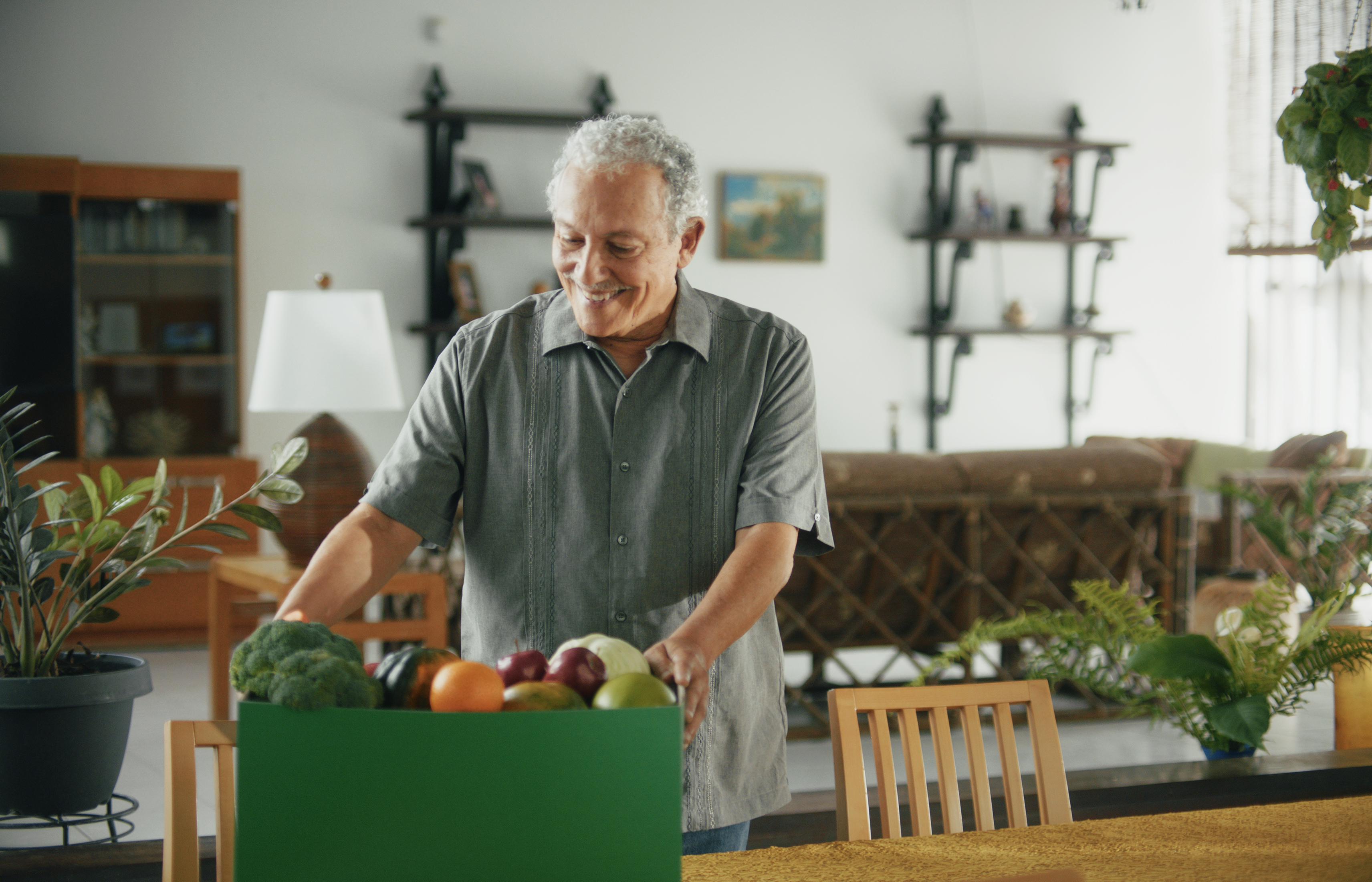 Older man smiling with a box of fresh food, fruits, and vegetables.